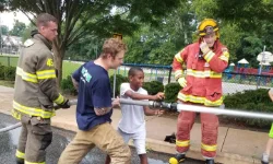 Two volunteers letting a father and son use the hose from the firetruck